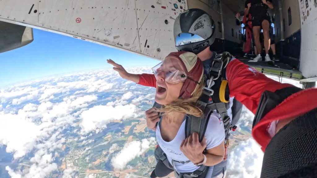 Tandemgast und Tandemmaster beim gemeinsamen Absprung aus dem Flugzeug über den Wolken