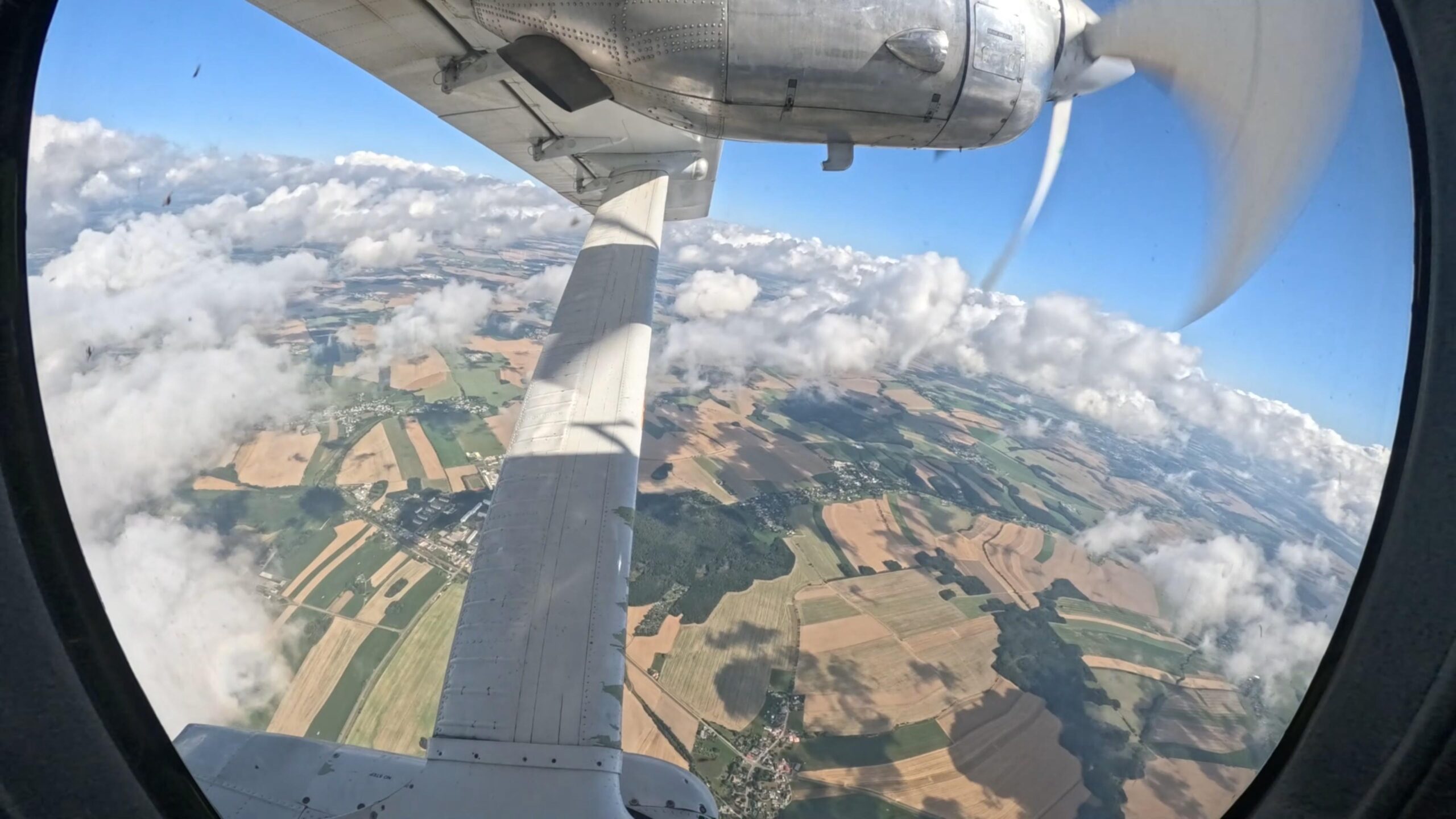 Blick aus dem Flugzeug auf Tragfläche, Propeller, Felder und Wolken während des Steigflugs