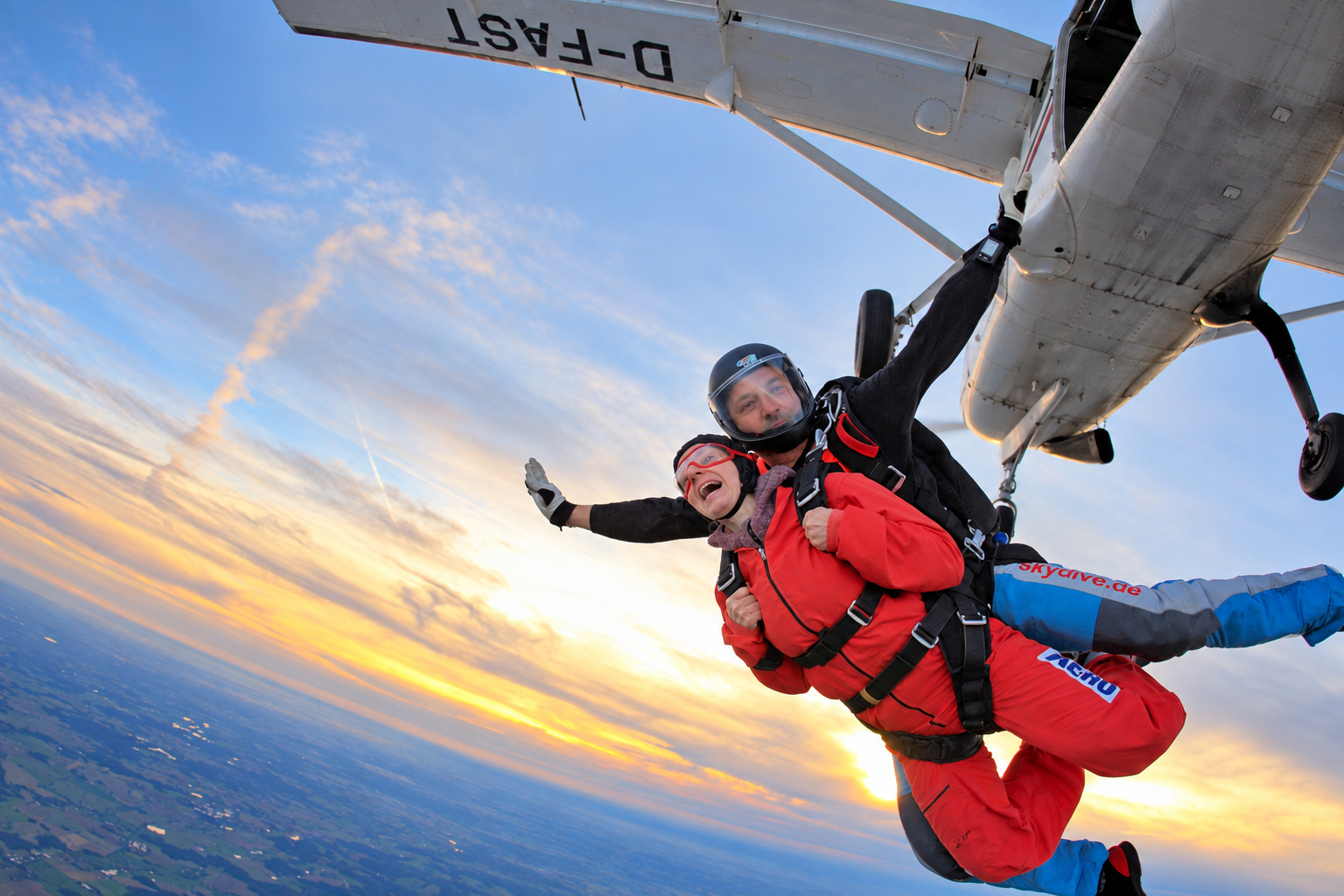 Tandemgast im roten Overall beim Absprung aus dem Flugzeug vor einem goldenen Abendhimmel