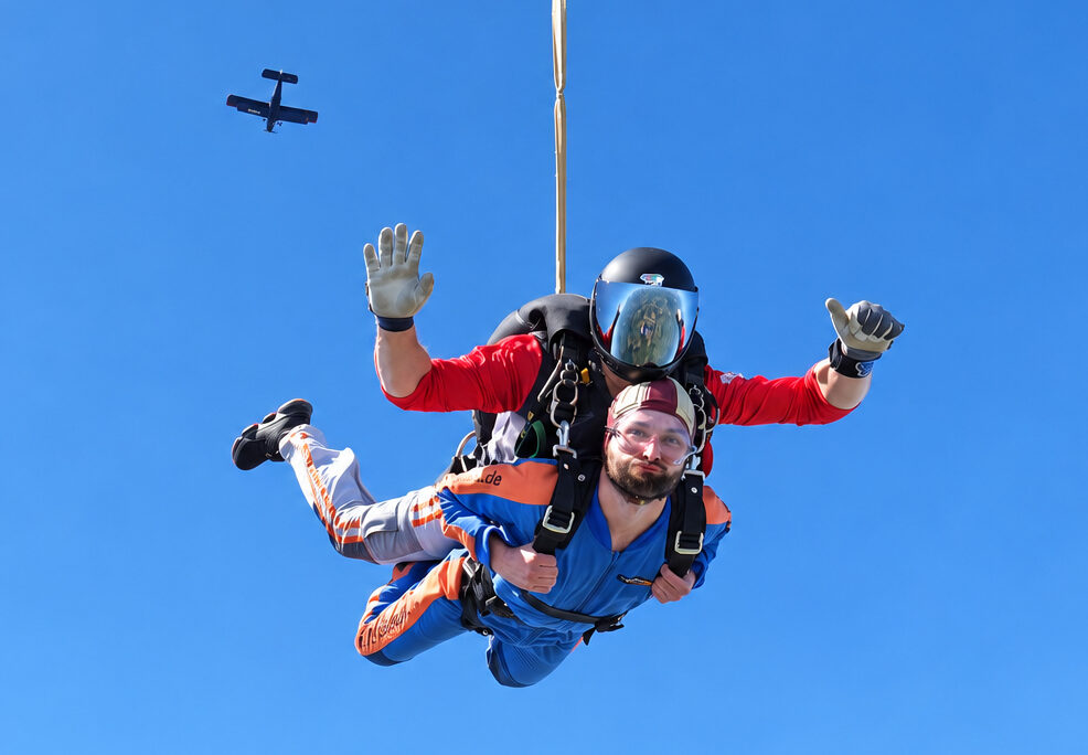 Tandemgast und Tandemmaster im freien Fall mit dem Flugzeug im blauen Himmel