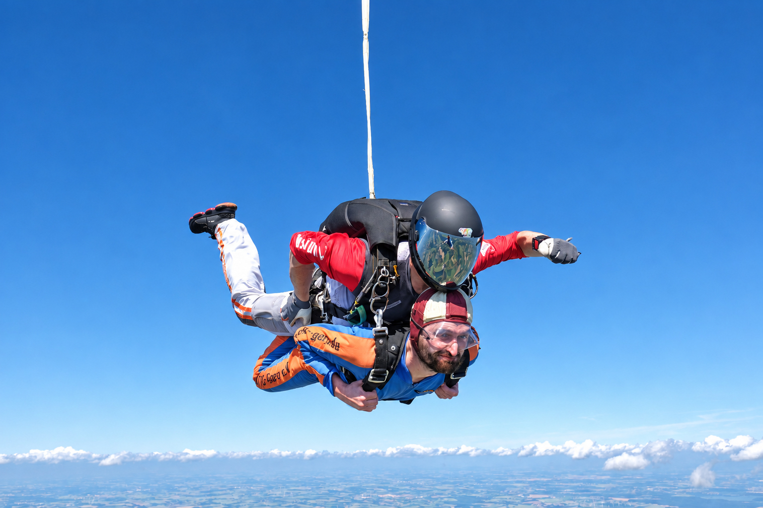 Tandemgast im blauen Overall und Tandemmaster im freien Fall über einem Wolkenhorizont