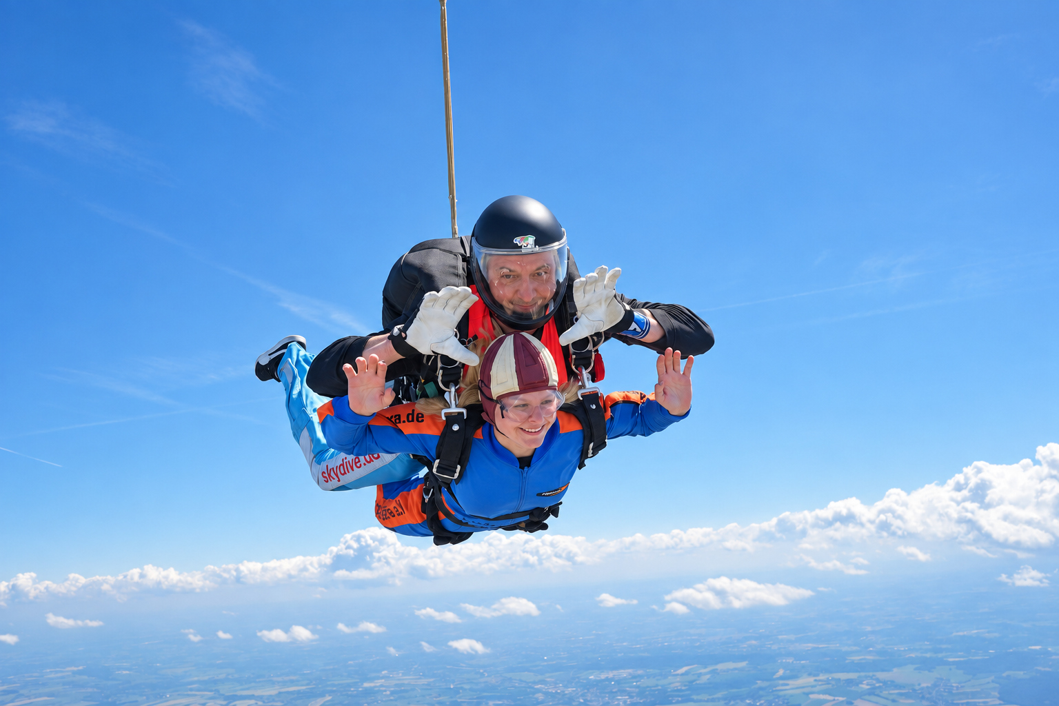 Lächelnder Tandemgast im blauen Overall mit Tandemmaster vor blauem Himmel und weißen Wolken